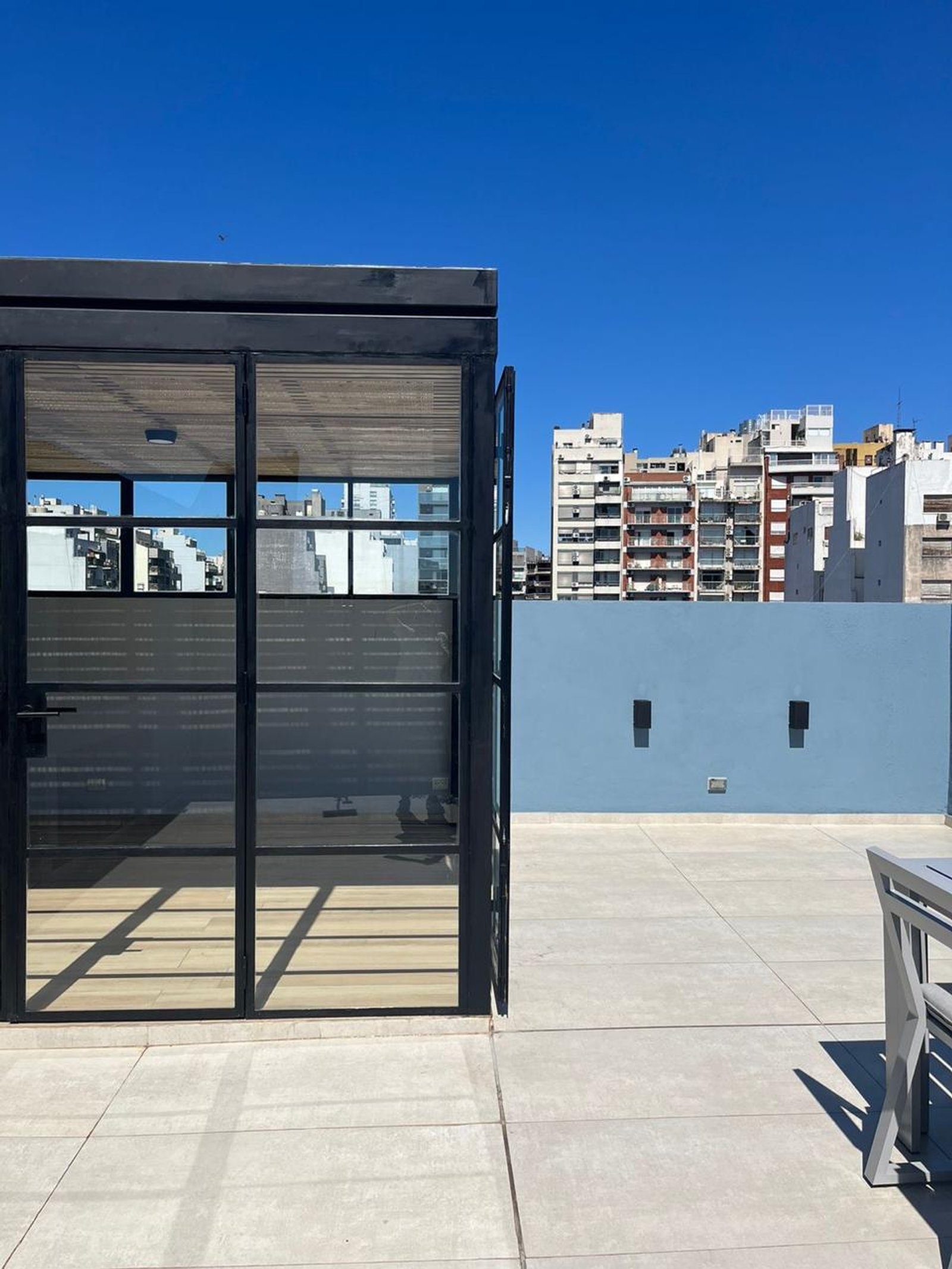 Terraza moderna con vista urbana, puertas de vidrio y pared azul — proyecto Gorriti , por Estudio NET Arquitectura , en Gorriti 3768